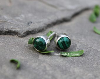 Puede incluir: Pendientes de botón plateados con piedras redondas de malaquita pulida. Los pendientes están sobre una superficie de piedra gris con hojas verdes. La malaquita tiene un distintivo patrón verde rayado.