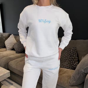 Puede incluir: Conjunto de sudadera y pantal&oacute;n de ch&aacute;ndal blanco con bordado azul. La sudadera dice "Wifey" y el pantal&oacute;n dice "14.08.2023".