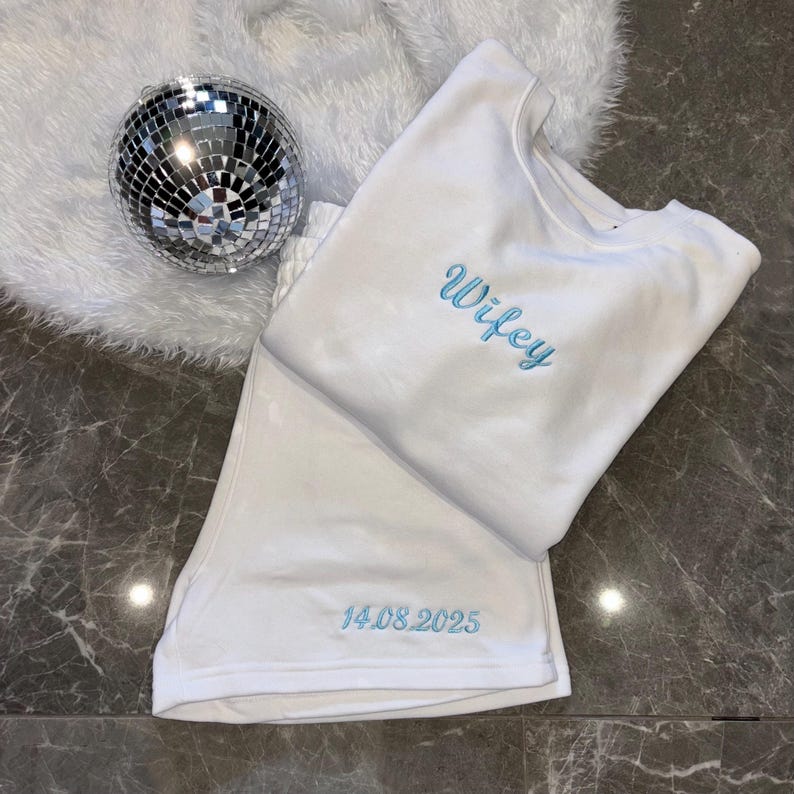 Puede incluir: Pijama de algod&oacute;n blanco con la palabra "wifey" bordada en azul en la parte superior y la fecha "14.08.2025" bordada en azul en la parte inferior.
