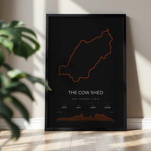 Könnte beinhalten: Ein gerahmtes schwarzes Poster mit dem orangefarbenen Umriss einer Radstrecke namens THE COW SHED. Unter der Karte steht ROAD, CLOCKWISE, 07.26.20, gefolgt von Daten für 102 KM, 535 M, 4:04:48, 2:24/KM und einem Höhenprofil-Diagramm.