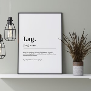 May include: A black and white printable poster with a definition of the word "lag" in a humorous way. The poster is framed and hanging on a white shelf with a potted plant.