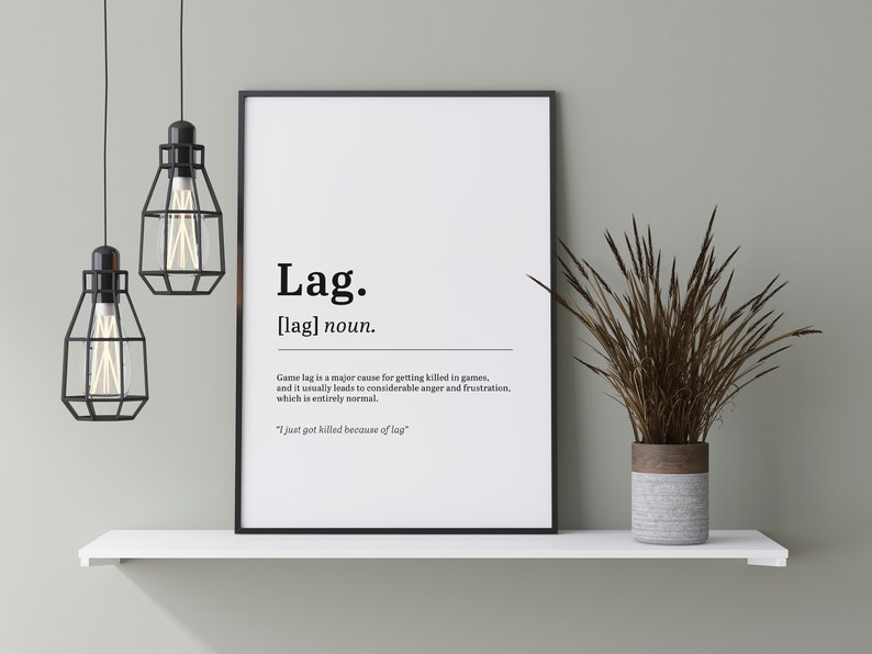 May include: A black and white printable poster with a definition of the word "lag" in a humorous way. The poster is framed and hanging on a white shelf with a potted plant.