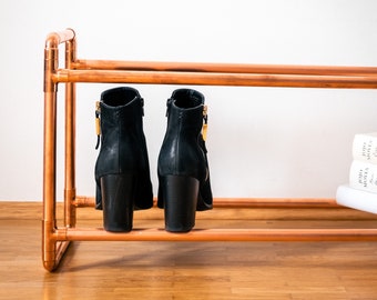 Hoge, industriële metalen schoenenrek, open, smal en ruimtebesparend, gemaakt van koperen buizen; moderne en industriële schoenenopslag.