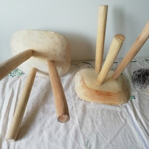 May include: Two unfinished wooden stools with three legs each. The stools are made of natural wood and have a rustic look.