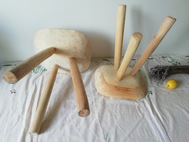 May include: Two unfinished wooden stools with three legs each. The stools are made of natural wood and have a rustic look.