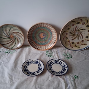 Op de afbeelding: Drie grote keramische borden met ingewikkelde, wervelende, veelkleurige patronen en twee kleinere witte keramische borden met een blauw bloemenrandontwerp. Een enkele gele citroen bevindt zich links van de grotere borden.