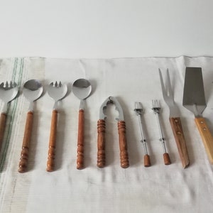 Könnte beinhalten: Ein Set aus acht Küchenutensilien mit Holzgriffen. Das Set enthält einen Servierlöffel, eine Serviergabel, einen Nussknacker, zwei kleine Gabeln, eine große Gabel und einen Spatel.