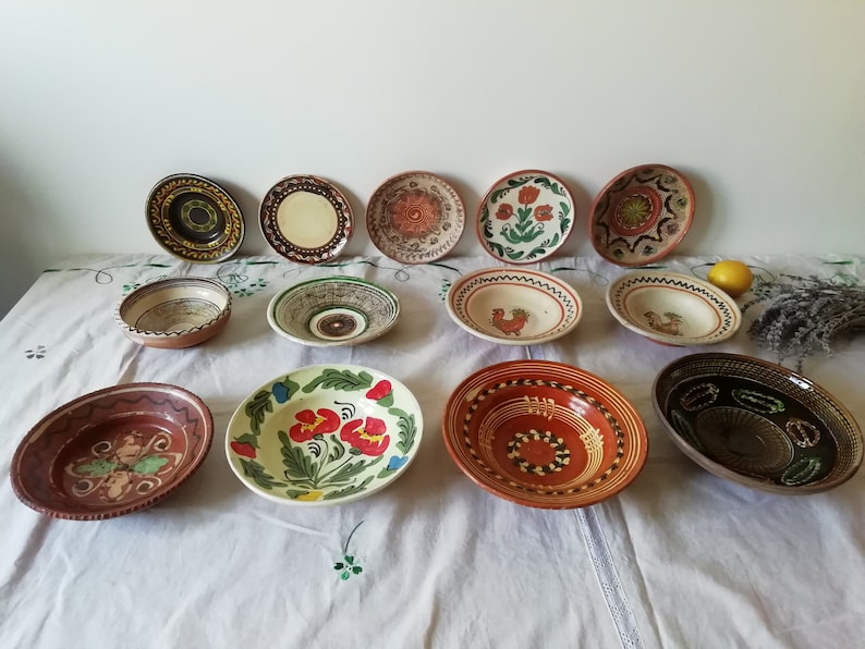 May include: A collection of 12 hand-painted ceramic bowls and plates with various floral and geometric designs. The bowls and plates are in shades of brown, red, green, yellow, and white.