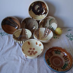 May include: A collection of eight ceramic bowls featuring various decorative patterns including marbled brown, black, and green swirls, as well as a bowl with brown polka dots and another with a brown and green striped rim design.