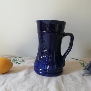 May include: A cobalt blue ceramic mug with a floral design. The mug has a wide base and a handle.