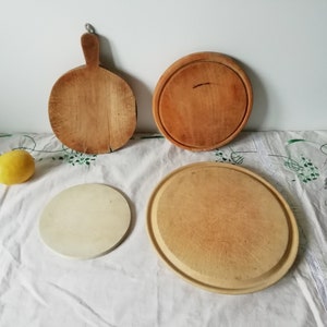 Puede incluir: Cuatro tablas de cortar redondas de madera, una con mango, sobre un mantel blanco con un limón y lavanda seca.