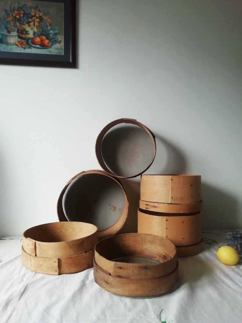 Może przedstawiać: Zestaw sześciu drewnianych sit do mąki w r&oacute;żnych rozmiarach. Sita wykonane są z naturalnego drewna i mają rustykalny, vintage'owy wygląd. Są ułożone jedno na drugim, z największym sitkiem na dole i najmniejszym na g&oacute;rze.