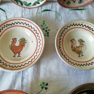 May include: Two white ceramic bowls with orange and green rooster designs. The bowls have a brown and black wavy border.
