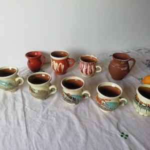 Peut inclure: Une collection de dix tasses en céramique avec différents motifs et designs colorés. Les tasses sont disposées sur une nappe blanche avec quelques brins de lavande en arrière-plan.