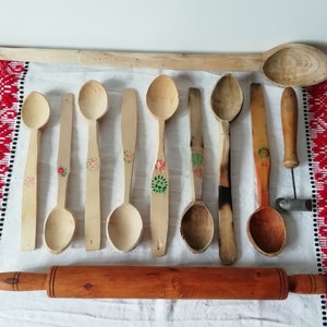 Può includere: Una collezione di cucchiai di legno con disegni dipinti, incluso un matterello. I cucchiai sono di diverse dimensioni e forme, alcuni con motivi floreali.