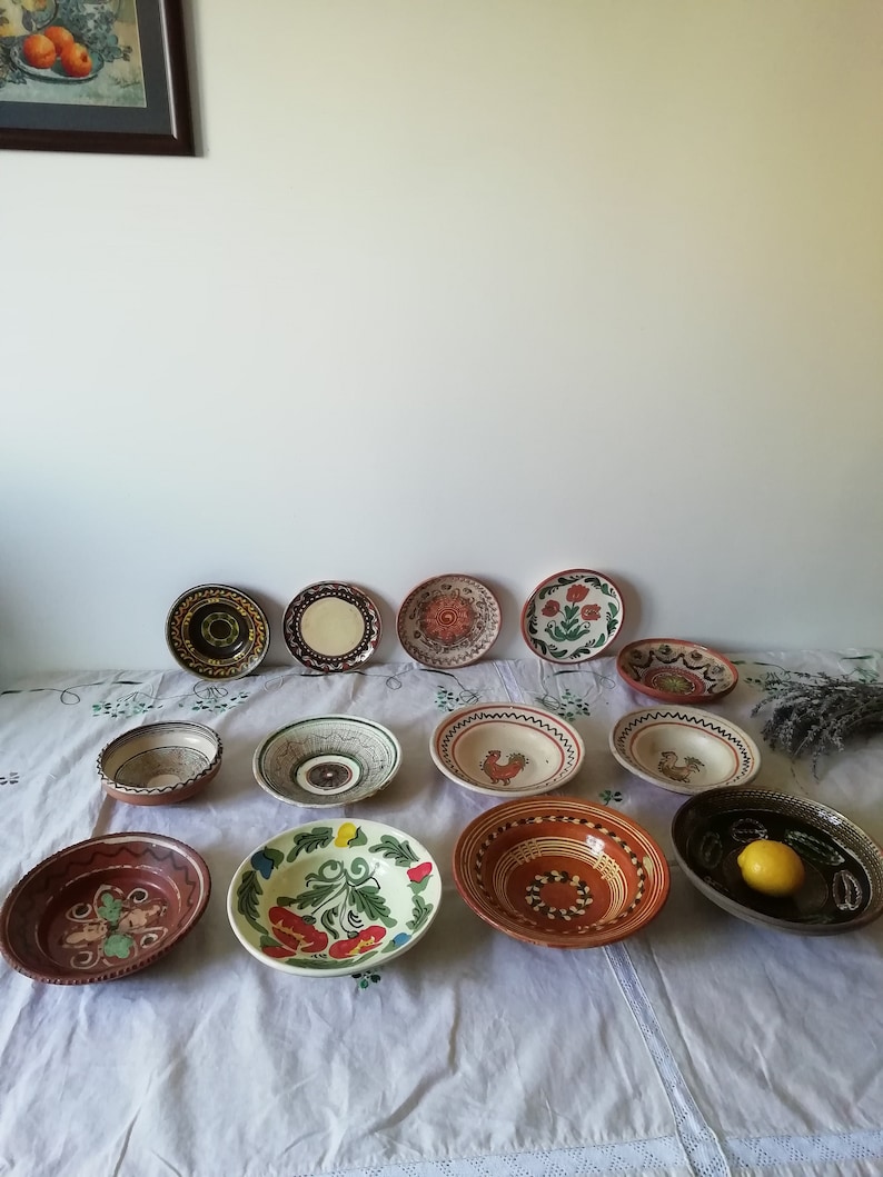 May include: A collection of 13 hand-painted ceramic bowls with various designs, including floral, geometric, and rooster motifs. The bowls are in shades of brown, red, green, blue, and white.