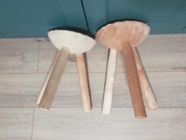 May include: Two wooden stools with three legs each. One stool has a white top and the other has a natural wood top.
