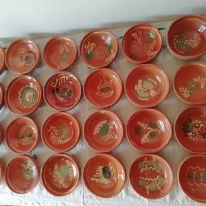 Puede incluir: Una colección de 20 cuencos de terracota con diseños florales pintados a mano en verde y blanco. Los cuencos son todos del mismo tamaño y forma, y están dispuestos en un patrón de cuadrícula.