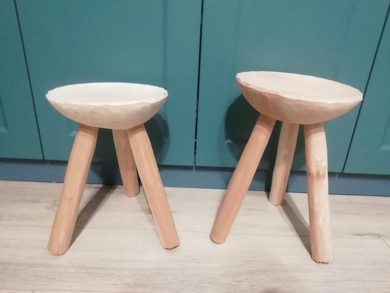 May include: Two wooden stools with three legs each. The stools are made of light wood and have a rounded top.