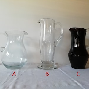 Könnte beinhalten: Drei Glaskrüge, einer klar, einer klar mit einem ausgestellten Boden und einer dunkelviolett.