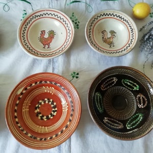 May include: Five ceramic bowls with different designs. The bowls are white, brown, and black with painted details. The designs include a rooster, a wreath, and geometric patterns.
