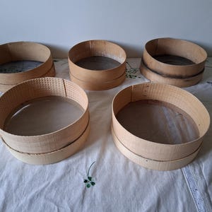 May include: Five wooden flour sifters of varying sizes, with a white background.