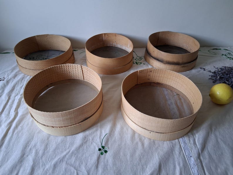 May include: Five wooden flour sifters of varying sizes, with a white background.