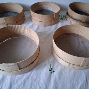 May include: Five wooden flour sifters with a mesh screen inside. The sifters are round and have a natural wood finish.