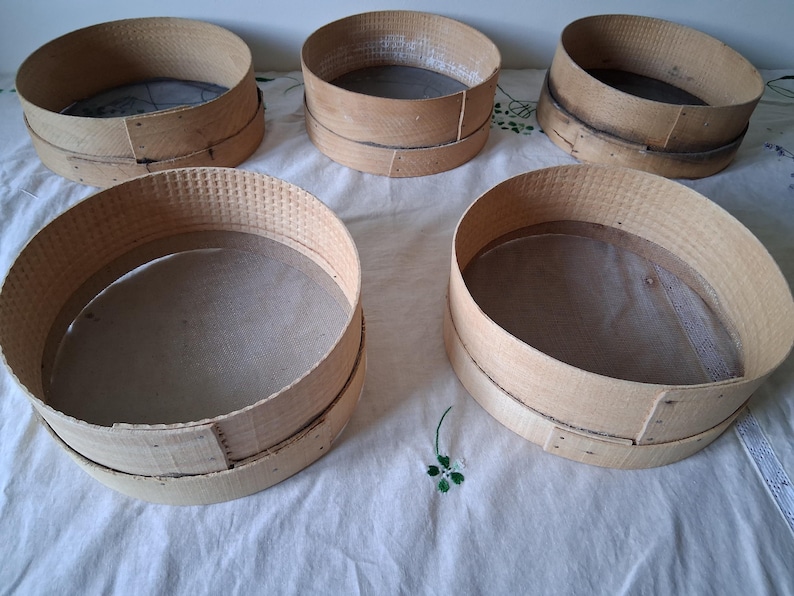 May include: Five wooden flour sifters with a mesh screen inside. The sifters are round and have a natural wood finish.