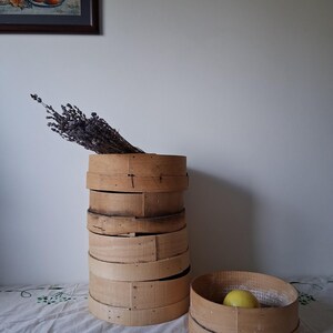 May include: A stack of wooden round baskets with a single basket on the side. The baskets are made of natural wood and have a rustic look. A bunch of dried lavender is in the top basket.