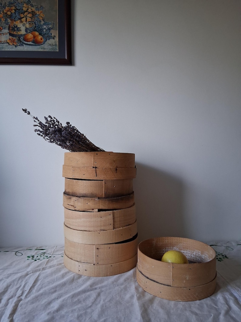 May include: A stack of wooden round baskets with a single basket on the side. The baskets are made of natural wood and have a rustic look. A bunch of dried lavender is in the top basket.