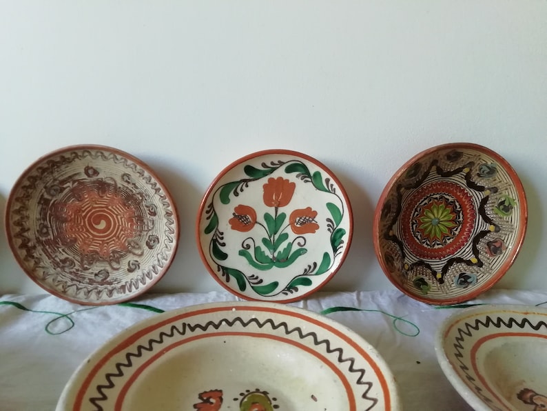 May include: Five ceramic plates with hand-painted designs. The plates are in various sizes and feature different patterns, including floral motifs, geometric shapes, and swirls. The plates are all in shades of brown, orange, green, and white.