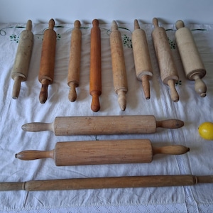 Puede incluir: Una colección de once rodillos de madera de diferentes longitudes, grosores y tonos de madera, dispuestos en filas. Los rodillos presentan cuerpos cilíndricos con mangos cónicos o redondeados. Un limón amarillo se encuentra a la derecha.