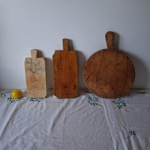 Puede incluir: Tres tablas de cortar de madera de diferentes formas y tamaños están dispuestas en fila. Una es de color claro y rectangular, otra es de color marrón medio y rectangular, y la tercera es de color marrón oscuro y circular. Un limón amarillo está a la izquierda.