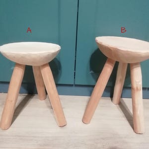 May include: Two wooden stools with three legs each. The stools are made of natural wood and have a simple, rustic design.