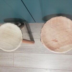 May include: Two wooden stools with a natural wood finish. The stools are round and have a slightly uneven surface. They are sitting on a light gray tiled floor.