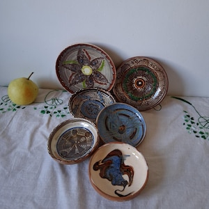 Peut inclure: Un ensemble de six bols en céramique ronds présentant divers motifs peints à la main dans des tons de bleu, marron, vert et crème. Les bols affichent des motifs complexes incluant des fleurs, des cercles concentriques et des tourbillons.