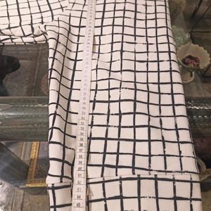 May include: White sweatshirt with a black grid pattern. The sweatshirt is measured with a tape measure, showing a length of approximately 70 inches. The garment has a ribbed hem and cuffs.