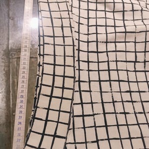 May include: Cream-colored fabric with a black grid pattern. A measuring tape is placed along the edge of the fabric, showing measurements from 15 to 42 inches. The fabric appears to be part of a garment or textile.