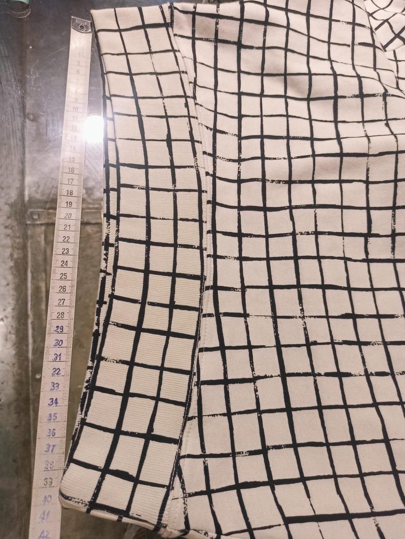 May include: Cream-colored fabric with a black grid pattern. A measuring tape is placed along the edge of the fabric, showing measurements from 15 to 42 inches. The fabric appears to be part of a garment or textile.