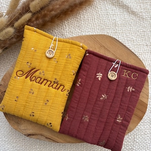 Peut inclure: Deux pochettes rectangulaires matelassées, l'une jaune moutarde avec un motif cerises et le mot Maman brodé en marron, l'autre bordeaux avec un motif feuilles et les initiales KC brodées en doré, toutes deux avec une fermeture à bouton en bois.
