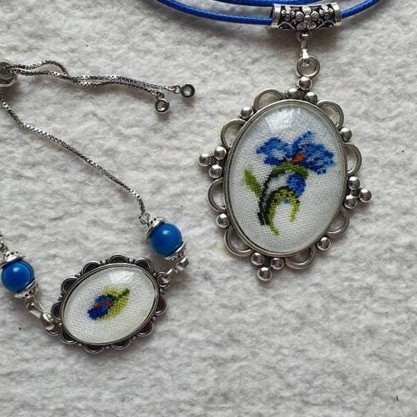 Pendentif et bracelet de couleur argent, motif iris bleue aux points de croix sous cabochon. Médaillon fleuri brodé