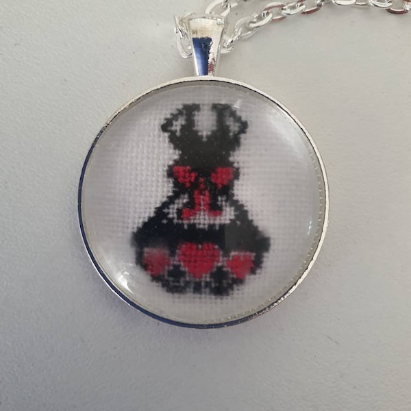 Pendentif petite robe noire et sa chaîne en argent 925. En broderie fine sous cabochon. Coeurs et ruban rose.