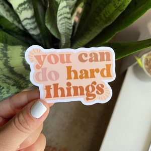 May include: A sticker with the text "You can do hard things" in a retro font style. The sticker is peach, orange, and brown with a white outline.