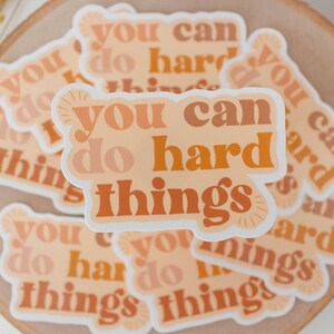 May include: A stack of stickers with the text "You can do hard things" in a retro font with orange, peach, and brown colors.