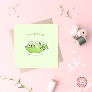 May include: A light green card with the text "Hap-pea Nikkah" and a cartoon illustration of two peas in a pea pod. The peas are smiling and have eyes and mouths. The card is on a light pink background.