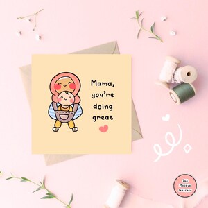 May include: A yellow card with a cartoon illustration of a woman wearing a headscarf carrying a baby. The text on the card reads "Mama, you're doing great" with a small pink heart.