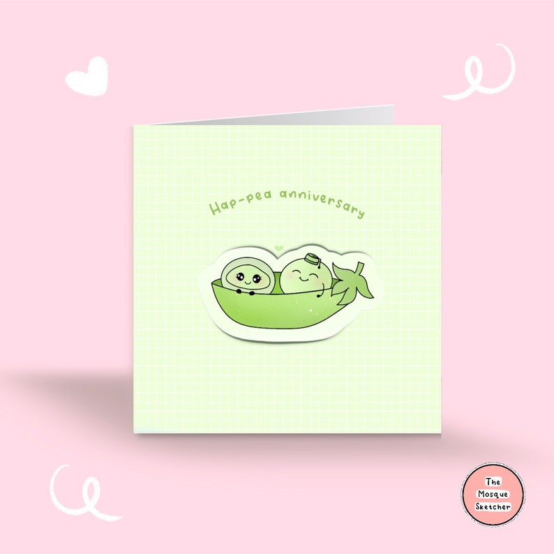 May include: A green card with a light green grid pattern. The card has the text "Hap-pea anniversary" in black. There is a sticker of two peas in a pod with faces and arms. The sticker is on a white background. The card has a small circle in the bottom right corner with the text "The Mosque Sketcher" in white.