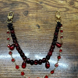 Deep crimson beads and gold chain details come together in this dark romantic purse charm, adding a bold statement to any handbag