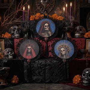 Puede incluir: Tres tapices circulares con figuras esqueléticas con velos y tocados ornamentados, enmarcados con encaje negro y borlas decorativas. Las ilustraciones muestran detalles de rostros de calavera sobre fondos de color azul y rojo.